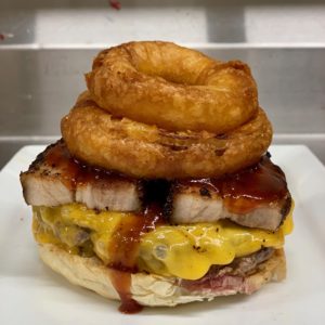 Half pound of fresh ground, hand packed angus beef topped with melting cheddar, brown sugar-coffee rubbed pork belly, sriracha honey bbq sauce and a stack of beer battered onion rings